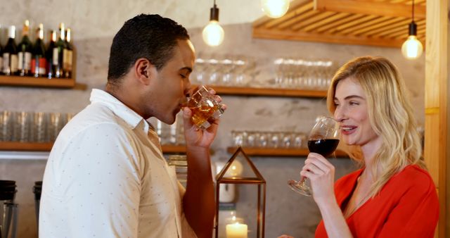 A middle-aged African American man and a Caucasian woman enjoy a wine tasting experience together, with copy space. Their smiles and the intimate setting suggest a casual yet romantic ambiance.
