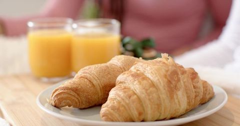 Friends sharing sunlit breakfast, enjoying croissants and orange juice