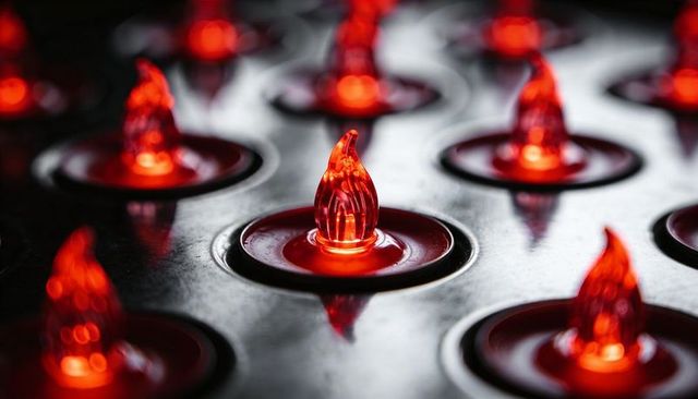 Glowing red led flame indicators in circular sockets on reflective black panel with bokeh