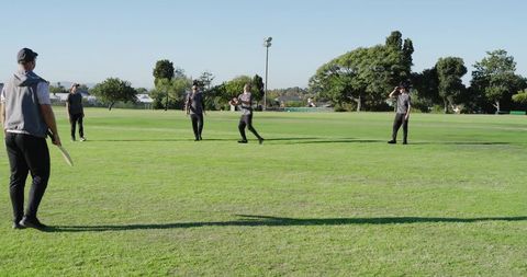 Teen cricket team training on sunny oval practicing batting and fielding drills