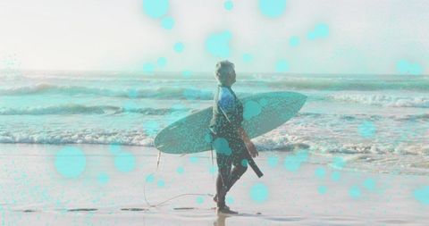 Active senior woman walking with surfboard on beach in full wetsuit, ocean surf lifestyle