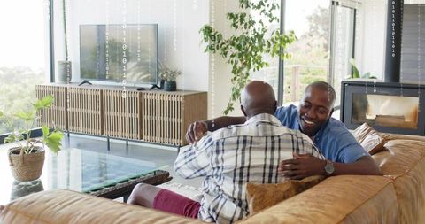 Adult son hugging father on leather couch sharing warm family embrace in modern living room