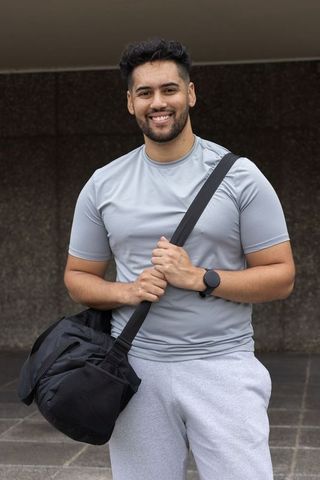 Smiling african american man carrying gym duffel wearing athletic gear and smartwatch