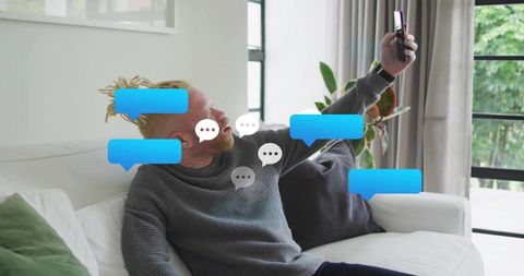 Young Man Relaxing on Sofa Communicating through Smartphone