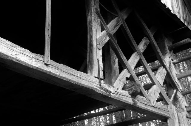 Close-up view of an abandoned old wooden structure in black and white, displaying its weathered beams and intricate frame. Perfect for illustrating rural architecture, history, decay, and rustic aesthetics. Useful for blogs, historical articles, rustic design projects, and stories about abandoned places.