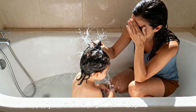 Mom bathing toddler in bathtub splashing water, playful bonding and caregiving moment