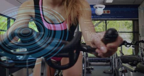 Female cyclist pedaling indoor spin bike wearing black tank pink trim with futuristic hud overlay
