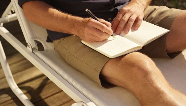 Man writing in notebook on sunlounger enjoying sunny patio journaling and note-taking