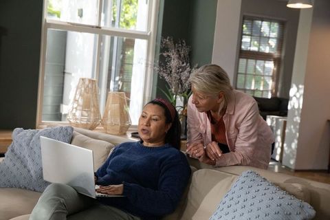 Mature women collaborating on laptop in sunlit contemporary living room