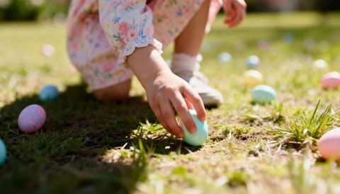 Toddler picking pastel easter egg in floral dress on sunlit spring lawn