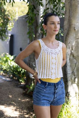 Sunlit garden fashion young woman standing in crochet tank and high-waist denim shorts