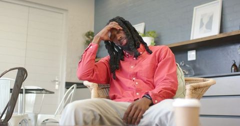 African american man sitting contemplative in wicker chair holding head with coffee cup