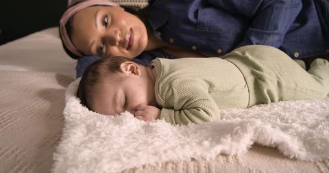 Mother resting with sleeping baby on cozy blanket