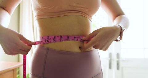 Asian woman measuring waist in comfortable activewear at home