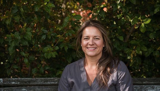 Smiling woman sitting on weathered bench in leafy park with warm autumn light