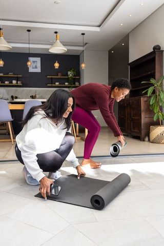 Diverse women preparing yoga mats in sunlit open-plan kitchen for home workout