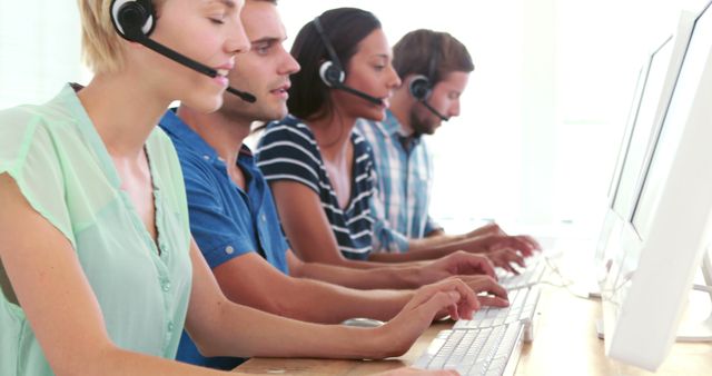 A diverse group of customer service representatives, wearing headsets, are working diligently at their computers, with copy space. Their focused expressions and professional attire suggest a busy call center environment.