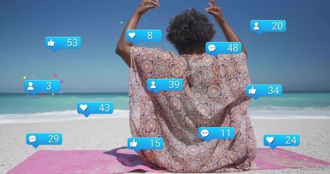 Senior woman celebrating on beach with social media reaction bubbles over turquoise ocean