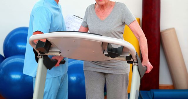 Senior woman receiving assistance from a physical therapist while working out on a treadmill. Ideal for depicting active aging, healthcare services, physical therapy practices, and senior fitness programs.