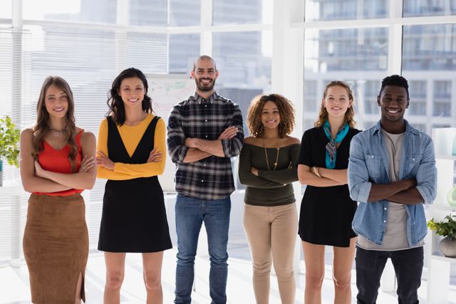 Diverse group of colleagues standing with arms crossed in a modern office. Ideal for use in business and corporate materials, team-building presentations, and workplace diversity promotions.