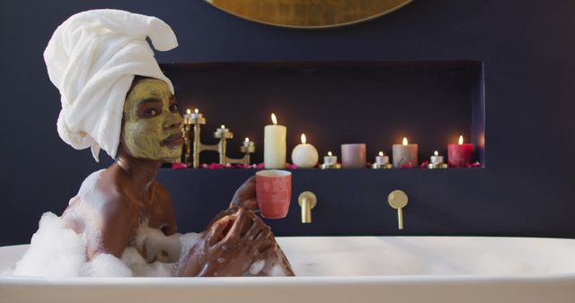 Smiling african american woman with towel and mask taking bath and drinking coffee in bathroom. health and beauty concept.