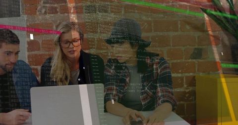 Software team collaborating on laptop with code overlay in brick wall office