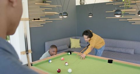 Friends playing pool in modern lounge, man lining up shot in mustard sweater