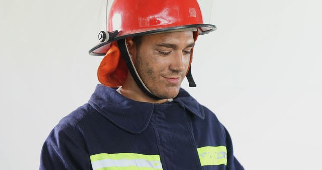 Happy biracial male firefighter wearing hardhat and protecting suit and looking down, copy space. Fire prevention, professionals, safety and expression concept, unaltered.