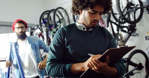 Mechanic writing on clipboard in busy bike workshop