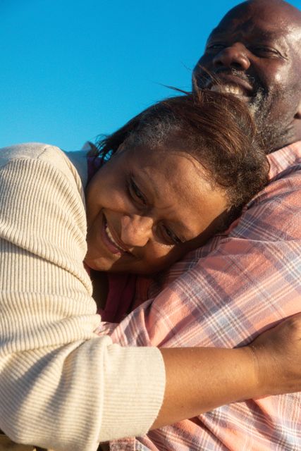 Happy affectionate african american senior woman embracing retired man at beach on sunny day. unaltered, love, togetherness, lifestyle, enjoyment and holiday concept.