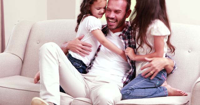 Happy Father Cuddling with Two Young Daughters on Couch - Download Free Stock Images Pikwizard.com