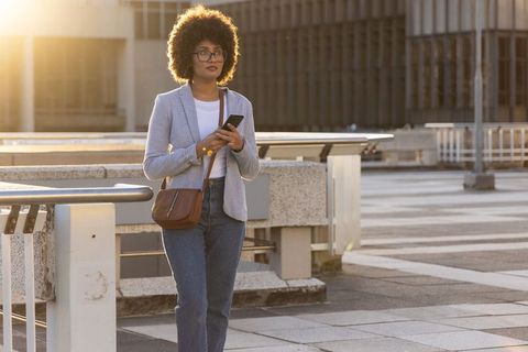 African american woman walking rooftop at golden hour with smartphone and crossbody bag
