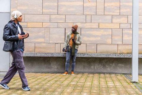 Walking and leaning with smartphones by urban wood-panel wall, street style, urban lifestyle