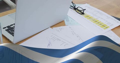 Minimal workspace featuring laptop, signed documents and reading glasses on wooden desk