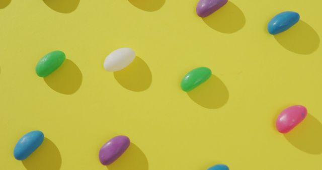Colorful jelly beans are arranged in a scattered yet organized pattern against a vibrant yellow background. This cheerful and bright image is perfect for marketing campaigns involving confectionery, playful designs, or materials needing a pop of color. Ideal for use in advertisements, social media posts, and web design to add a fun and energetic touch.