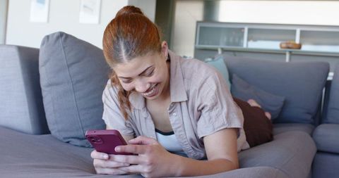 Young woman relaxing on sectional sofa using smartphone and smiling, casual lifestyle