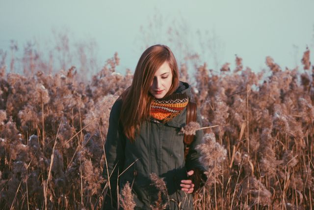 Young woman exploring autumn field in warm clothing, suggesting themes of tranquility, nature connection, and seasonal fashion. Ideal for use in lifestyle, nature, and fashion contexts, promoting outdoor activities, seasonal clothing, or peaceful moments in nature.