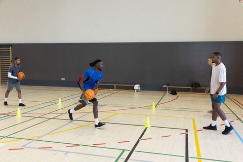 Male teammates practicing basketball dribbling drill in indoor gymnasium