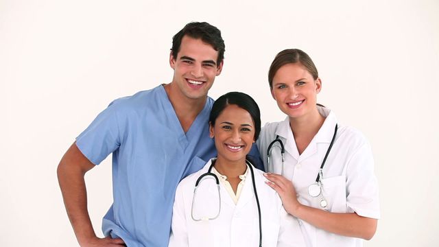 This video depicts a group of doctors standing together against a plain white background. They are smiling, showing a sense of camaraderie and teamwork. This video can be used on healthcare websites, brochures, and medical publications to depict professionalism, diversity, and a positive work environment in the healthcare sector.