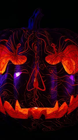 Vertical video of pulsing carved pumpkin revealing vine filigree grin in Halloween glow
