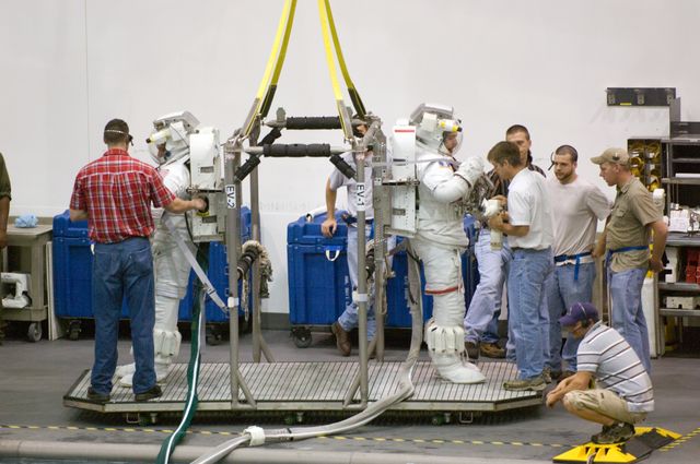 Astronauts are seen preparing for underwater training in the Neutral Buoyancy Laboratory (NBL) near Johnson Space Center. Wearing training versions of the Extravehicular Mobility Unit (EMU) spacesuits, the astronauts are getting ready to simulate a spacewalk. This setting at NASA emphasizes the meticulous preparation required for space missions. This image is ideal for use in publications or presentations related to space exploration, astronaut training, advanced technologies, and teamwork.