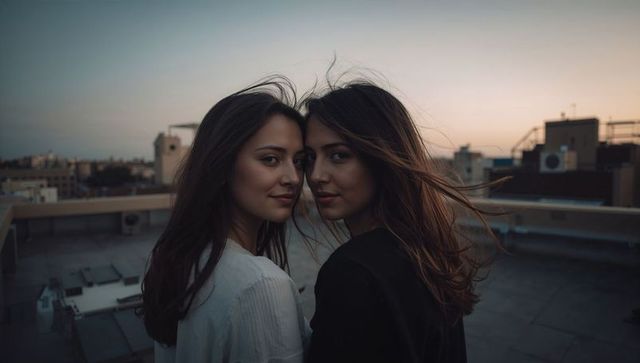 Two women standing on rooftop at dusk facing camera windblown hair urban twilight portrait