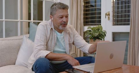Senior Man Video Calling on Laptop Wearing Earbuds at Home