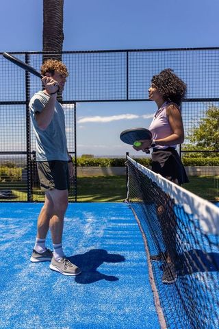 Mixed-race players standing at net playing pickleball on vibrant blue court under sunny sky