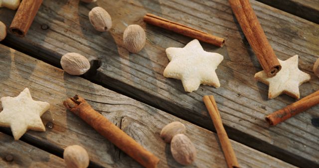 Star-shaped cookies are interspersed with cinnamon sticks and nutmeg on a rustic wooden surface, with copy space. The arrangement suggests a cozy, festive atmosphere, often associated with holiday baking and seasonal flavors.