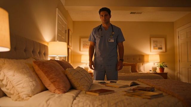 Male healthcare worker standing in warm bedroom in scrubs and stethoscope with open books