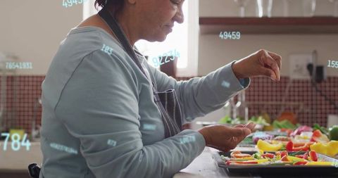 Senior woman seasoning colorful vegetables on baking tray in home kitchen with digital overlay