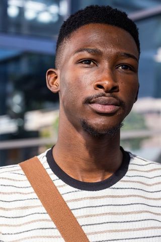 Thoughtful african young man looking up wearing striped sweater and brown bag strap urban headshot