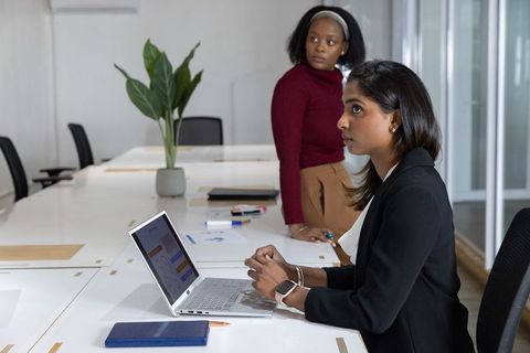 Diverse female colleagues collaborating on laptop in modern meeting room with plants