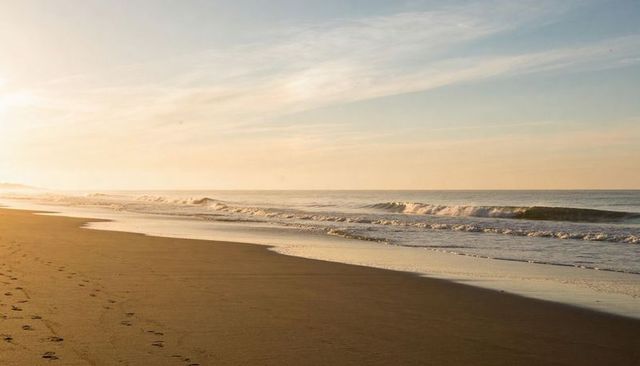 Golden sunrise calm beach with footprints and gentle waves on solitary sandy shoreline